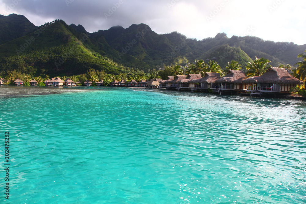 View towards the a bay in Moorea, with turquoise tropical water & bungalows over the sea. French Polynesia, South Pacific.