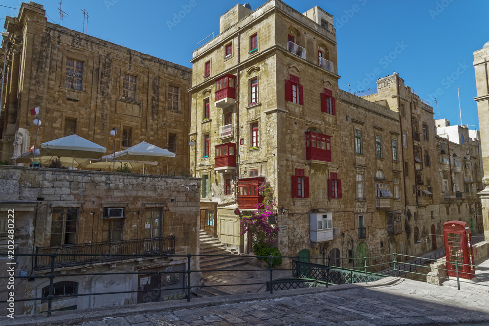 Valletta, Malta Traditional buildings with red balconies. Day view of Maltese limestone buildings with British phone booth in the streets of the capital of Malta.