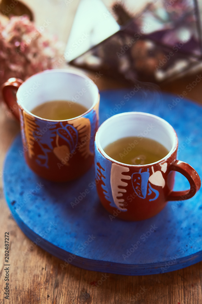 Two red cups with tea stand on a blue plate with florarium behind them Two red cups with tea stand on a blue plate with florarium behind them