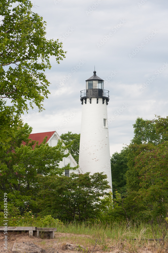 The Point Iroquois Lighthouse viewed through some trees., the building is white, with a red roof