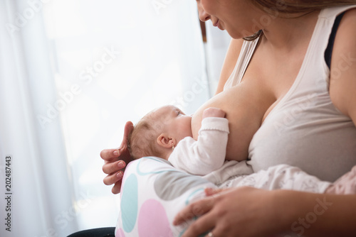 mother breastfeeding baby girl in white interior