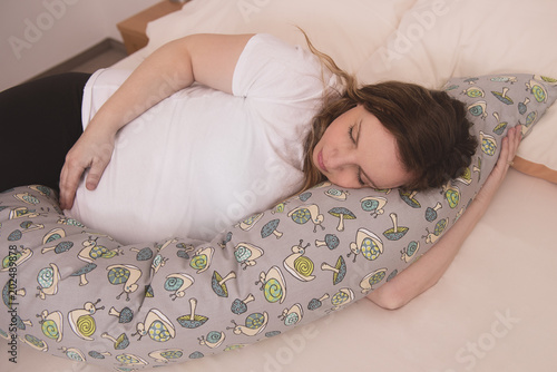 Pregnant woman laying on a bed sleeping with pregnancy pillow