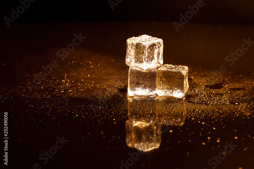 Golden ice cubes reflection on black table.
