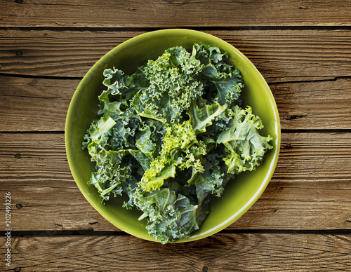Kale in green bowl over wooden background