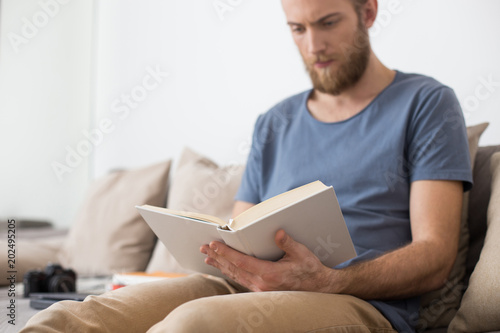 Close up photo of man sitting on gray sofa and thoughtfully reading book at home isolated