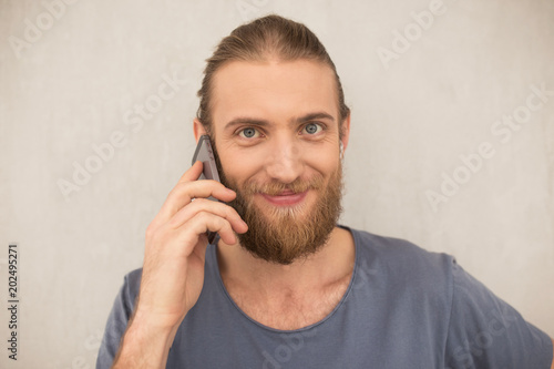 Portrate of young man with beard standing and talking on his cellphone while happily looking in camera isolated