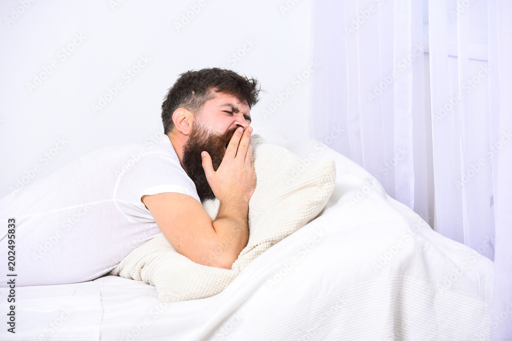 Man in shirt yawning while laying on bed, white wall and curtain on background. Sleepyhead concept. Guy on sleepy tired face yawning. Macho with beard and mustache yawning, relaxing, having nap, rest. Man in shirt yawning while laying on bed, white wall and curtain on background. Sleepyhead concept. Guy on sleepy tired face yawning. Macho with beard and mustache yawning, relaxing, having nap, rest.