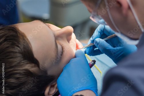 Teenager in a dental clinic. A dentist is treating teeth with tools.