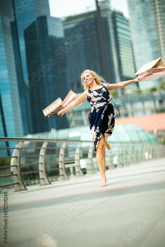 The Joy of Shopping... Excited Beautiful Woman on air, wearing casual blue dress with flowers, shopping bags in the streets with skyscrapers