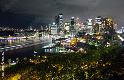 Wide view of Sydney CBD cityscape at night with light trails from ferry traffic in Circular Quay