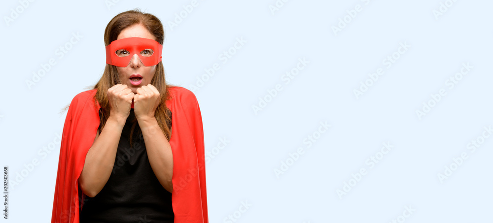 Middle age super hero woman wearing red mask and cape terrified and nervous expressing anxiety and panic gesture, overwhelmed isolated blue background Middle age super hero woman wearing red mask and cape terrified and nervous expressing anxiety and panic gesture, overwhelmed isolated blue background