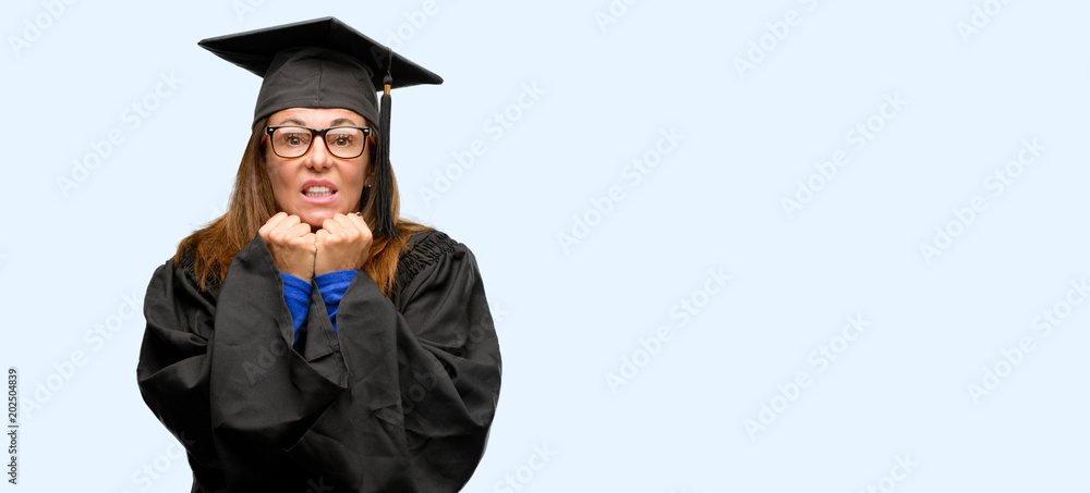 Senior graduate student woman terrified and nervous expressing anxiety and panic gesture, overwhelmed isolated blue background Senior graduate student woman terrified and nervous expressing anxiety and panic gesture, overwhelmed isolated blue background