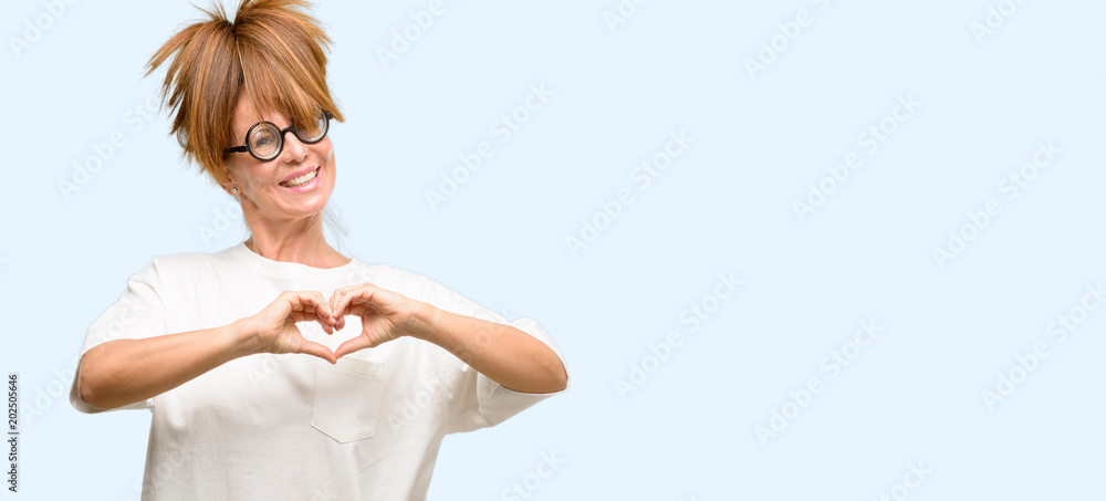 Obraz premium Crazy middle age woman wearing silly glasses happy showing love with hands in heart shape expressing healthy and marriage symbol isolated blue background