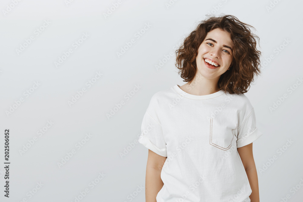Inviting us come and dinner together. Portrait of positive friendly-looking attractive girlfriend in white t-shirt, smiling broadly and expressing good attitude while talking casually with coworkers