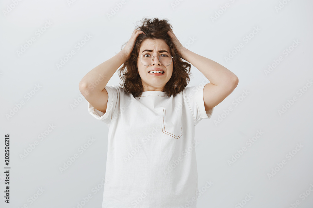 Girl realises how hard being grown-up. Indoor shot of troubled good-looking woman with short curly hair, feeling anxious and nervous, grimacing from confusion, making huge mistake over gray wall Girl realises how hard being grown-up. Indoor shot of troubled good-looking woman with short curly hair, feeling anxious and nervous, grimacing from confusion, making huge mistake over gray wall
