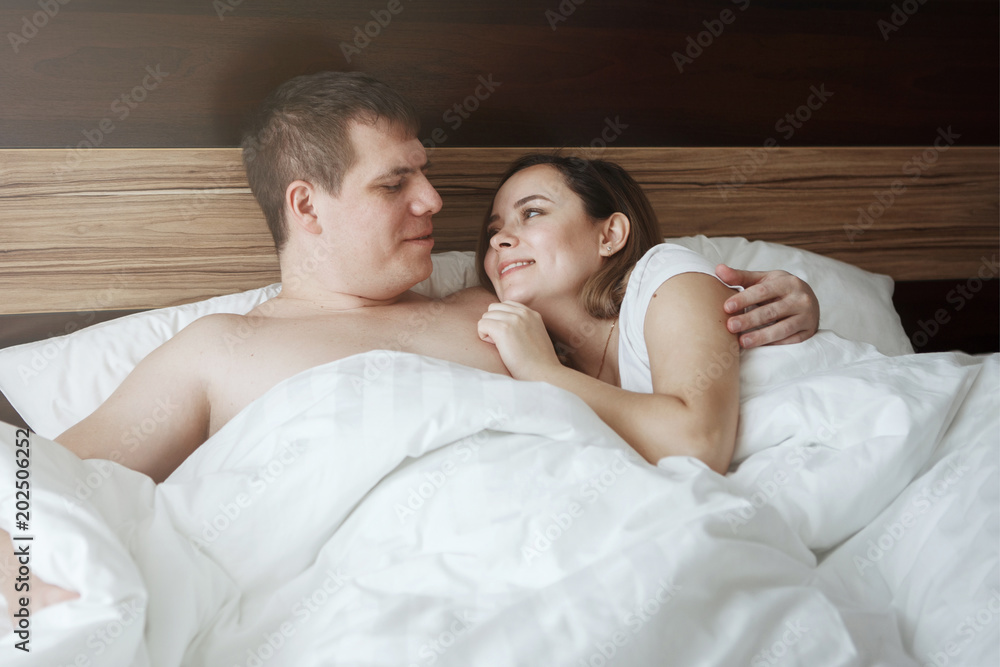 Young beautiful husband and wife resting in bed under a white blanket in a hotel room Young beautiful husband and wife resting in bed under a white blanket in a hotel room