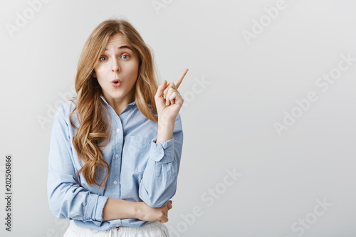Great suggestion came to girl mind. Studio portrait of attractive creative european female raising index finger and having wow, being excited and amazed, recalling memory or having idea over gray wall photo