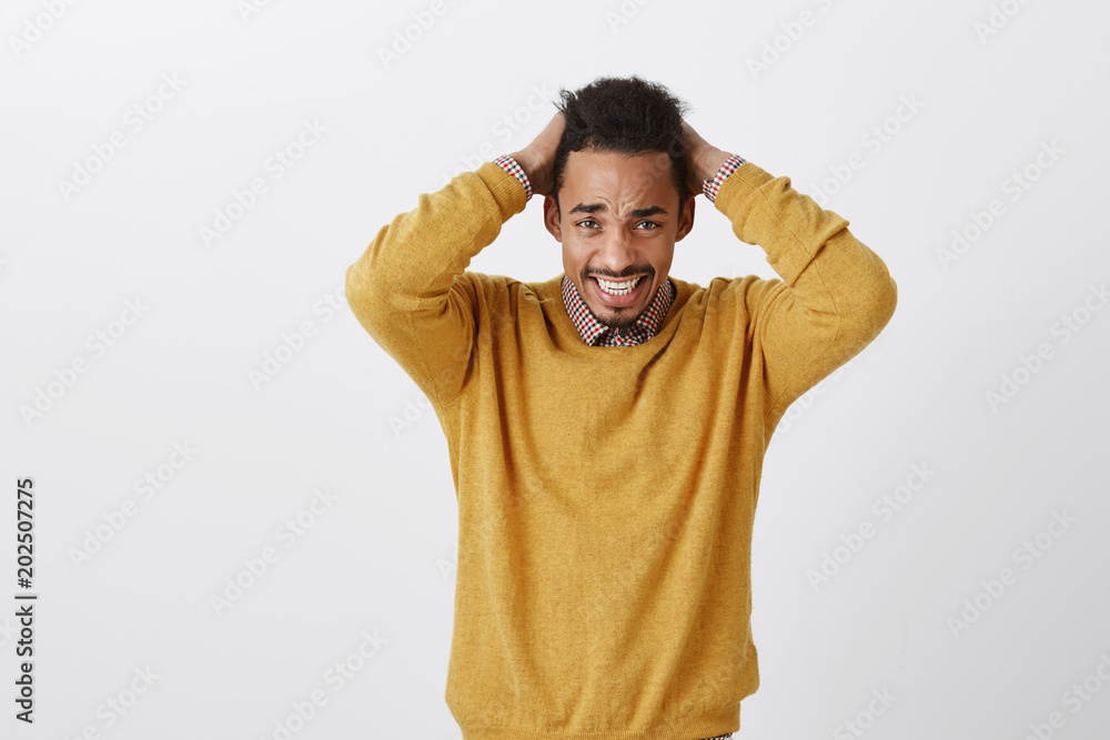 Disaster happened with poor student. Displeased frustrated young dark-skinned man with afro haircut holding hands behind head, suffering from emotional pain, frowning from dispair and sadness Disaster happened with poor student. Displeased frustrated young dark-skinned man with afro haircut holding hands behind head, suffering from emotional pain, frowning from dispair and sadness