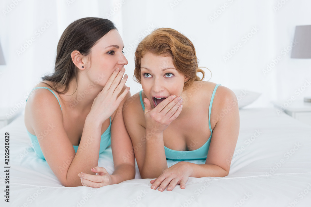 Female friends in tank tops gossiping in bed Female friends in tank tops gossiping in bed