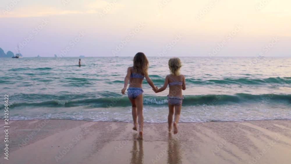 Two little girls run to the sea at sunset. Slow motion