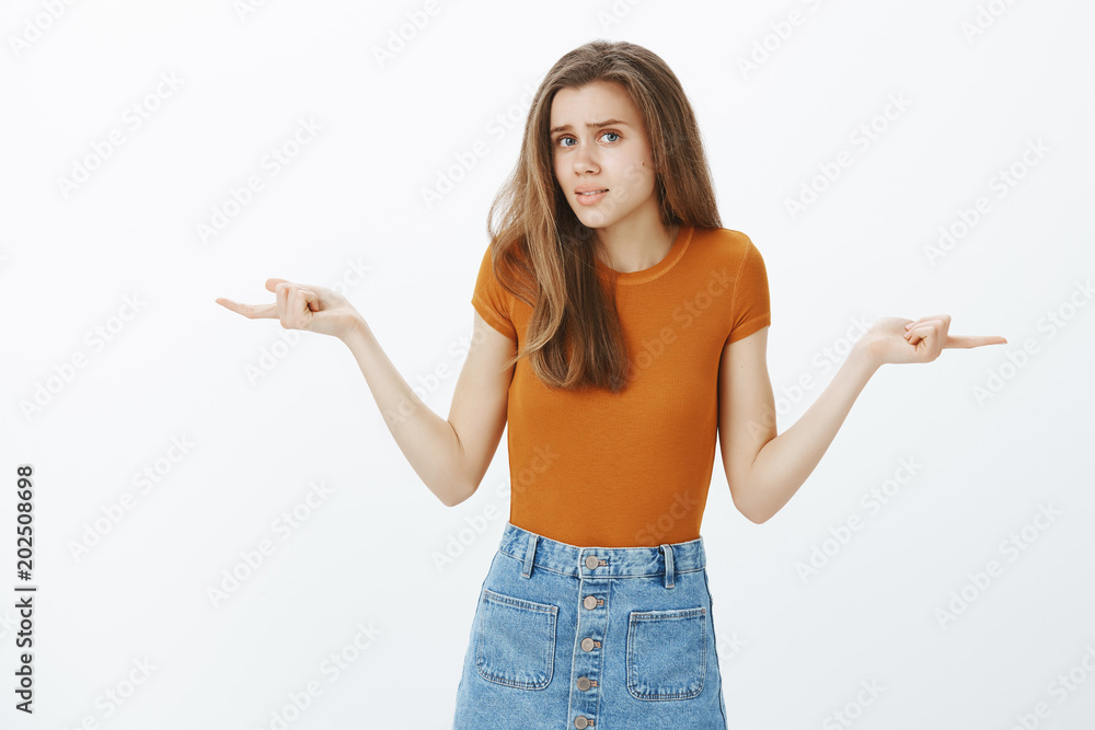 Complicated good-looking slender girlfriend with blond hair, spreading hands and pointing left and right with confused and questioned expression, being unware where to go over gray background Complicated good-looking slender girlfriend with blond hair, spreading hands and pointing left and right with confused and questioned expression, being unware where to go over gray background