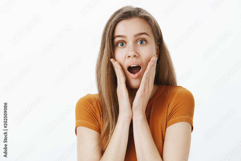 Waist-up shot of impressed surprised attractive female student in trendy outfit, dropping jaw, saying wow and holding palms near opened mouth, being astonished with amazing thing over gray background Waist-up shot of impressed surprised attractive female student in trendy outfit, dropping jaw, saying wow and holding palms near opened mouth, being astonished with amazing thing over gray background