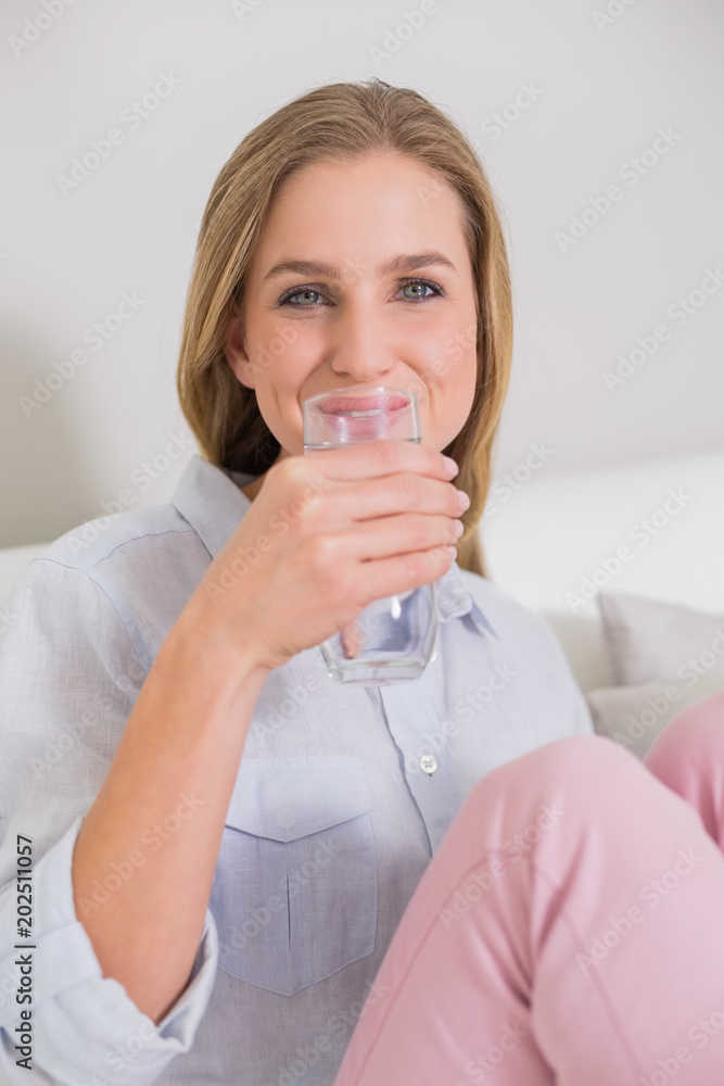Happy casual blonde sitting on couch drinking water Happy casual blonde sitting on couch drinking water