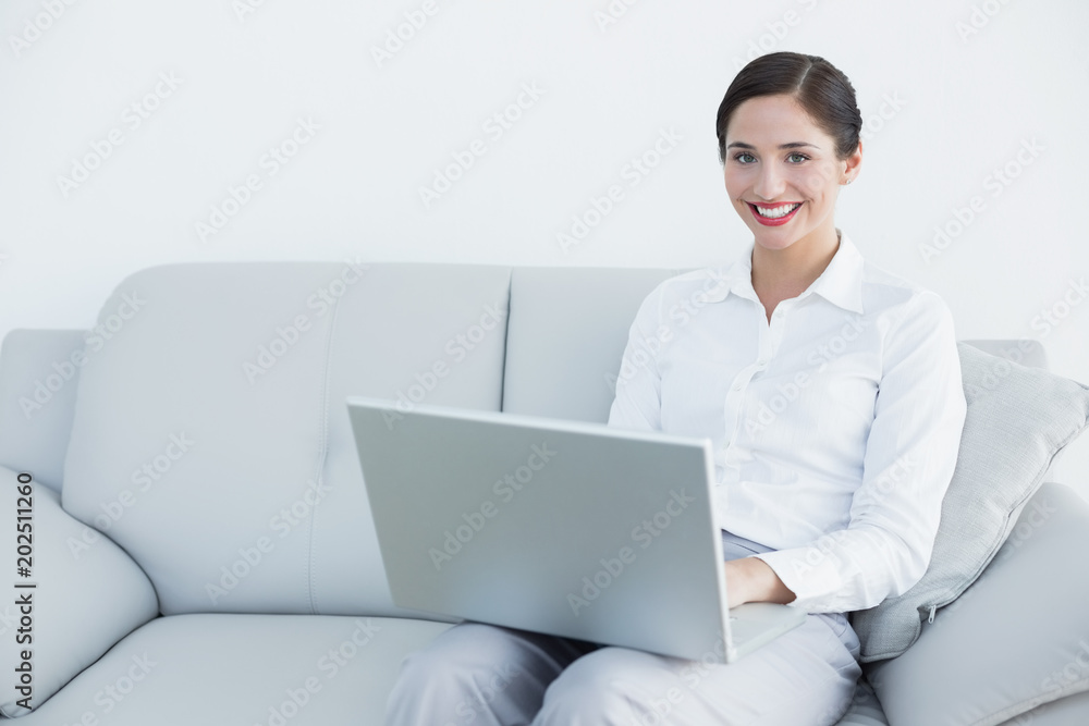 Smiling well dressed young woman using laptop on sofa Smiling well dressed young woman using laptop on sofa