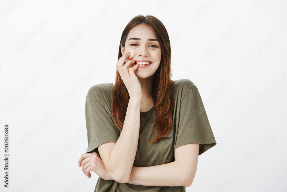 Studio shot of grinning attractive european woman in casual t-shirt, biting finger sensually, feeling temptation and happiness while taking part in curious event, standing over gray background Studio shot of grinning attractive european woman in casual t-shirt, biting finger sensually, feeling temptation and happiness while taking part in curious event, standing over gray background