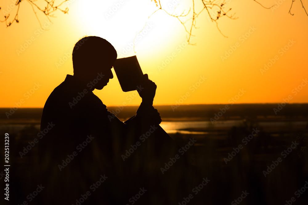 Φωτογραφία silhouette of a young man with a Bible, male praying to God in nature, the conce