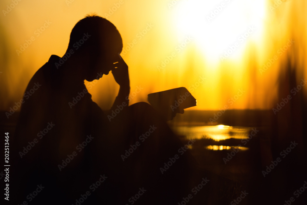 Φωτογραφία silhouette of a young man with a Bible, male praying to God in nature, the conce