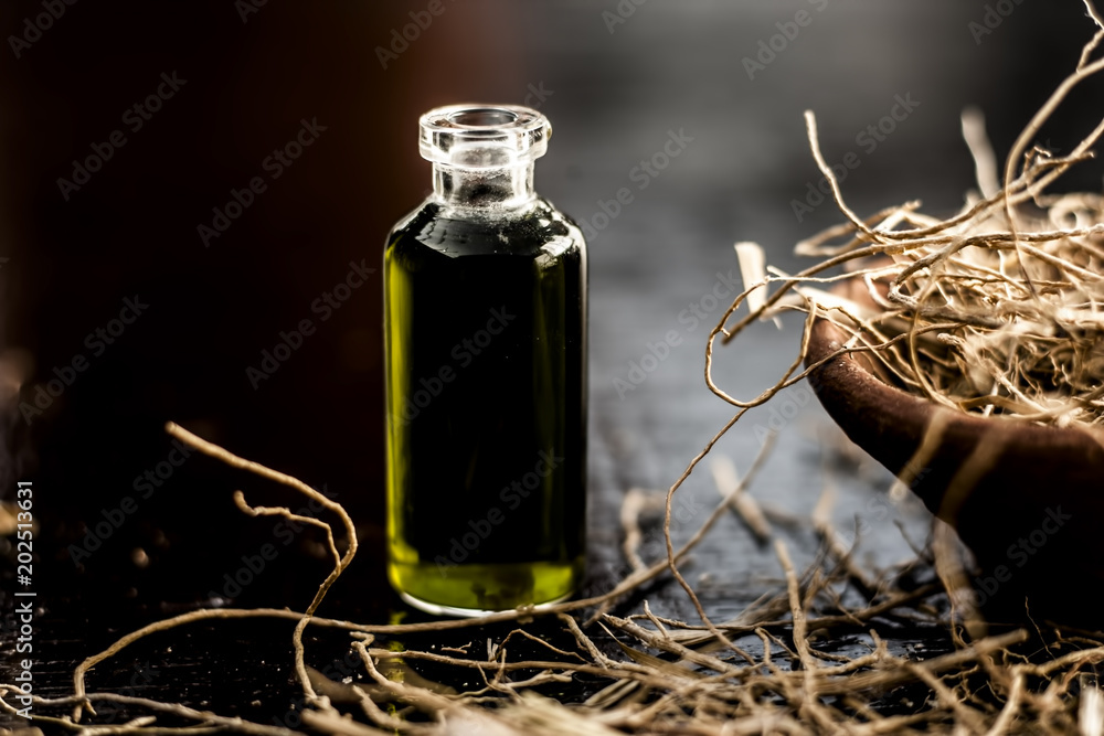 Φωτογραφία Floral and ayurvedic essence of herb Vetiver grass or Khus in a transparent bottle used in many beverages of Indian and Asia with dried vetiver grass in a clay bowl on black surface