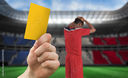 Hand holding up yellow card against stadium full of france football fans with player