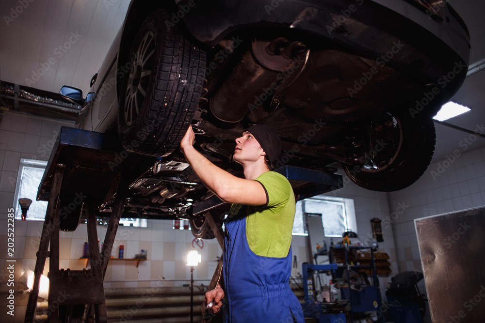 Φωτογραφία A young man makes an inspection of the running gear of a defective car on a scissor lift