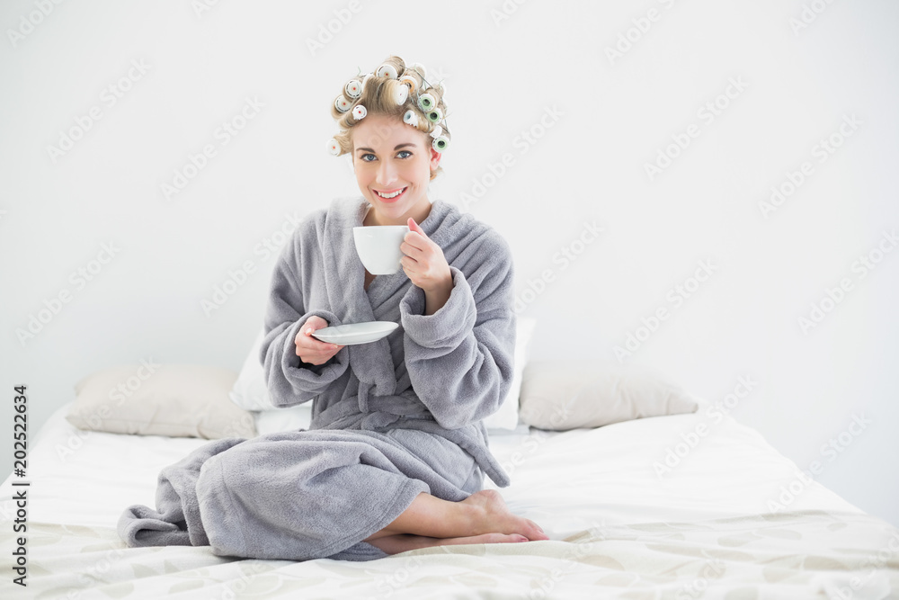 Cheerful relaxed blonde woman in hair curlers drinking coffee Cheerful relaxed blonde woman in hair curlers drinking coffee