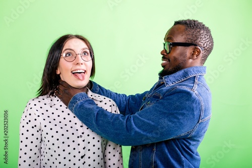 Vászonkép African man jokingly strangles a girl with a protruding tongue on a green backgr