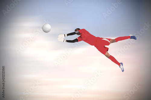 Goalkeeper in red making a save against beautiful blue cloudy sky