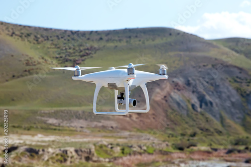 Drone quad copter with high resolution digital camera on the sky .White drone with digital camera flying in sky over mountain Drone with high resolution digital camera.