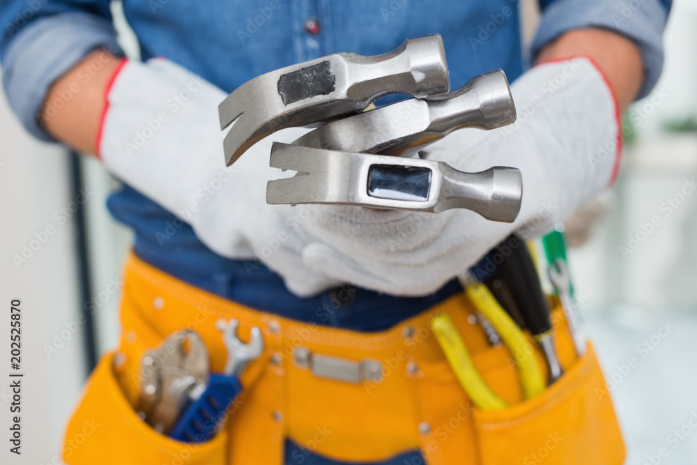 Mid section of handyman holding hammers with toolbelt around waist Mid section of handyman holding hammers with toolbelt around waist