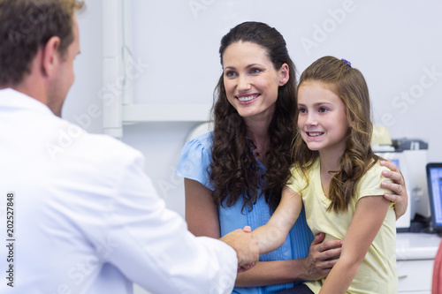 Dentist shaking hand with daughter after dental examination