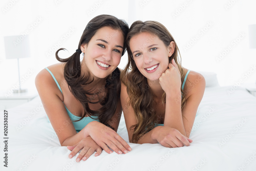 Smiling young female friends lying in bed