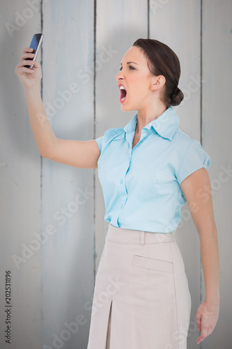 Angry classy businesswoman yelling at her smartphone against painted blue wooden planks