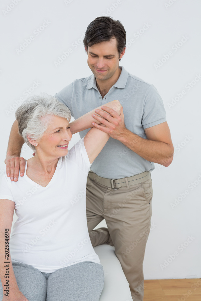 Fototapeta premium Physiotherapist stretching a smiling senior womans arm