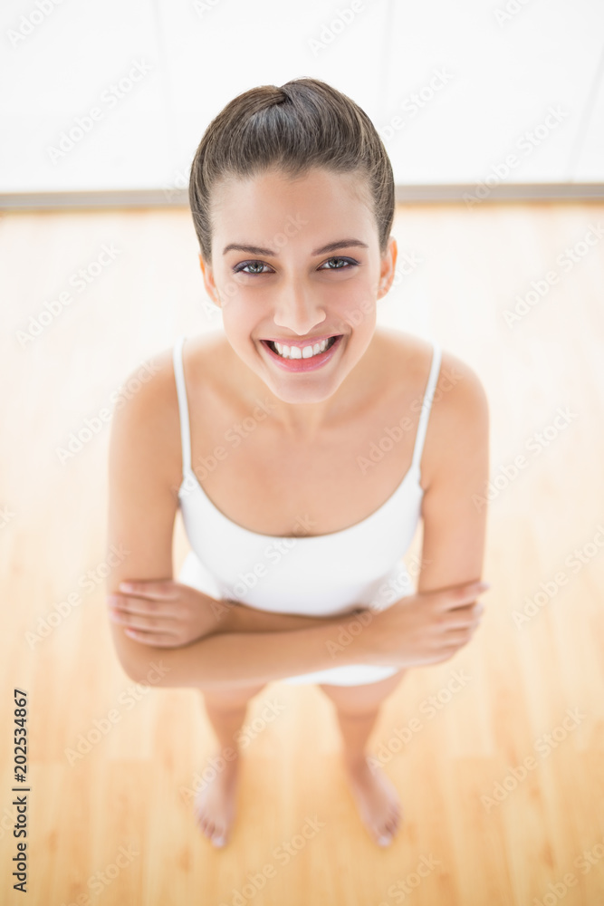 Attractive natural brown haired woman in white sportswear posing with arms folded