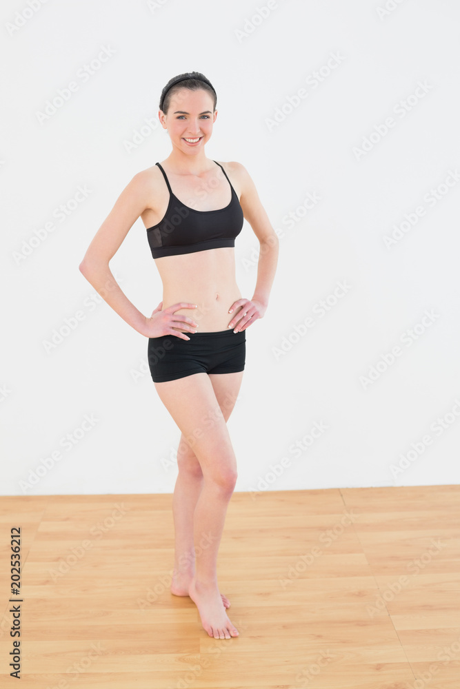 Smiling toned woman with hands on hips in fitness studio