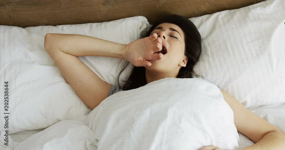Close up from above of the beautiful young brunette woman waking up in the sunny morning, yawning and smiling. Indoor Close up from above of the beautiful young brunette woman waking up in the sunny morning, yawning and smiling. Indoor
