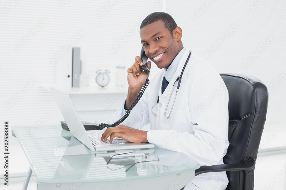 Smiling doctor using phone and laptop at medical office Smiling doctor using phone and laptop at medical office