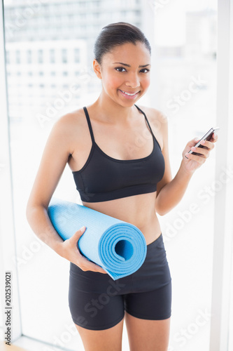 Cheerful dark haired model in sportswear carrying an exercise mat and a mobile phone © WavebreakmediaMicro