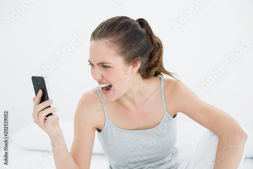 Woman shouting into mobile phone in bed