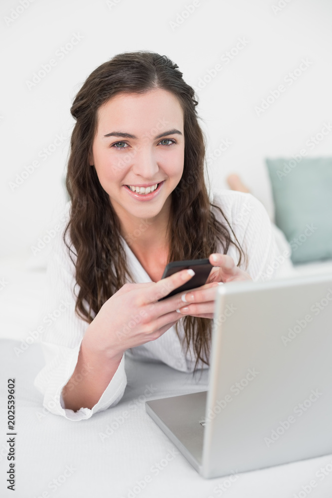 Smiling casual woman with cellphone and laptop in bed Smiling casual woman with cellphone and laptop in bed